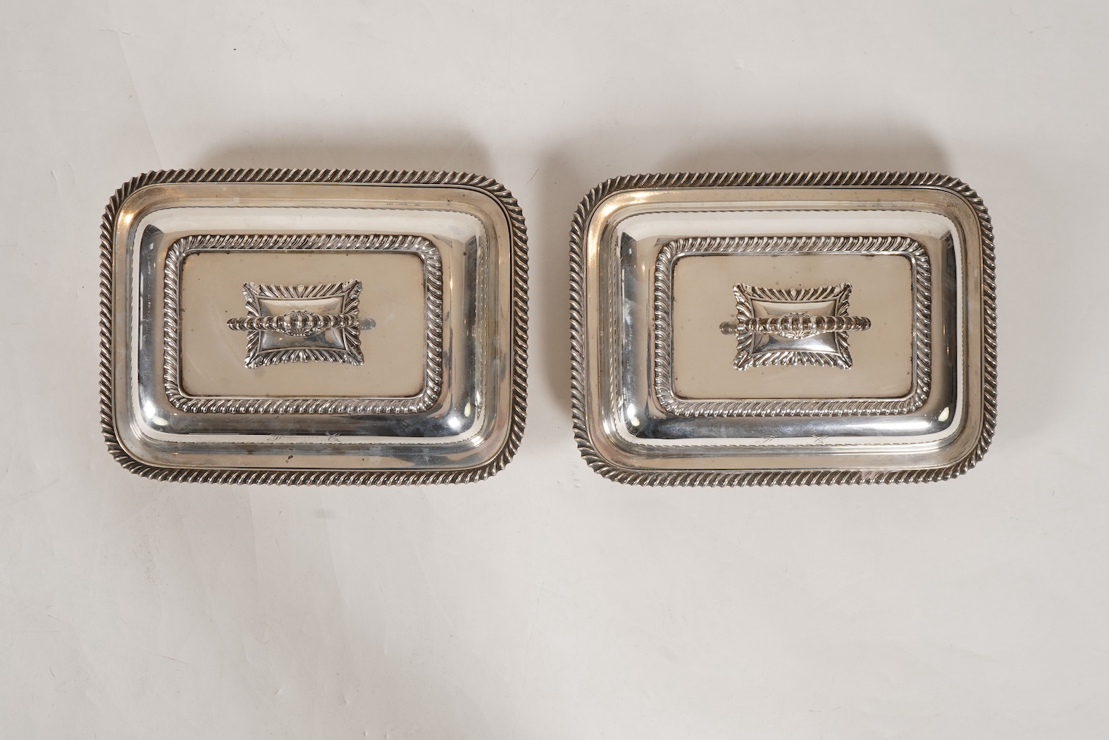 A matched pair of George V silver rectangular entrée dishes and covers, both with gadrooned borders and similar unmarked handles, Ellis & Co, Birmingham, 1923 and Ellis & Co, Birmingham, 1932, base 27.8cm, 108.3oz, exclu